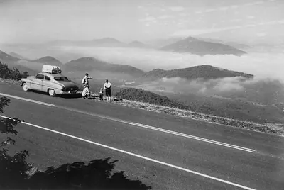 Travelers beside a parked car at a misty mountain overlook