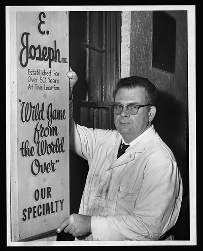 Man in white coat beside E. Joseph, Inc. sign
