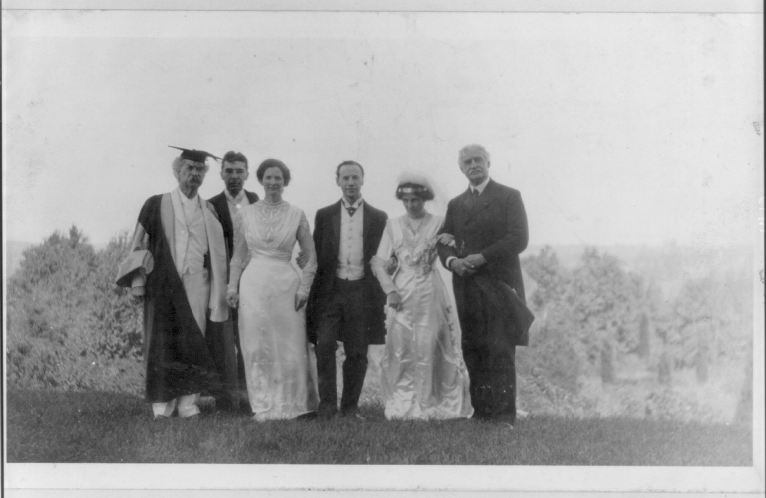 [Samuel Langhorne Clemens, 1835-1910, full-length portrait, standing, facing right, wearing cap and gown, with 5 other people at the wedding of Clara Clemens] — historic photograph
