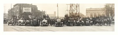 Panoramic street photo of uniformed men beside early automobiles