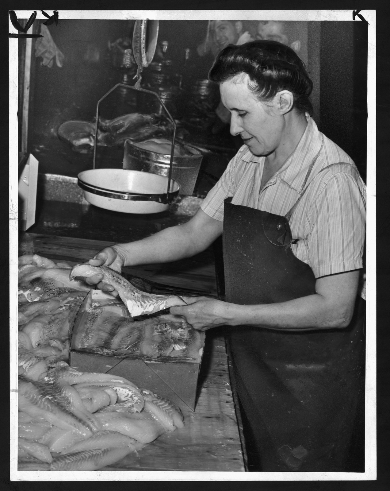 Woman filleting fish at a market counter — historic image