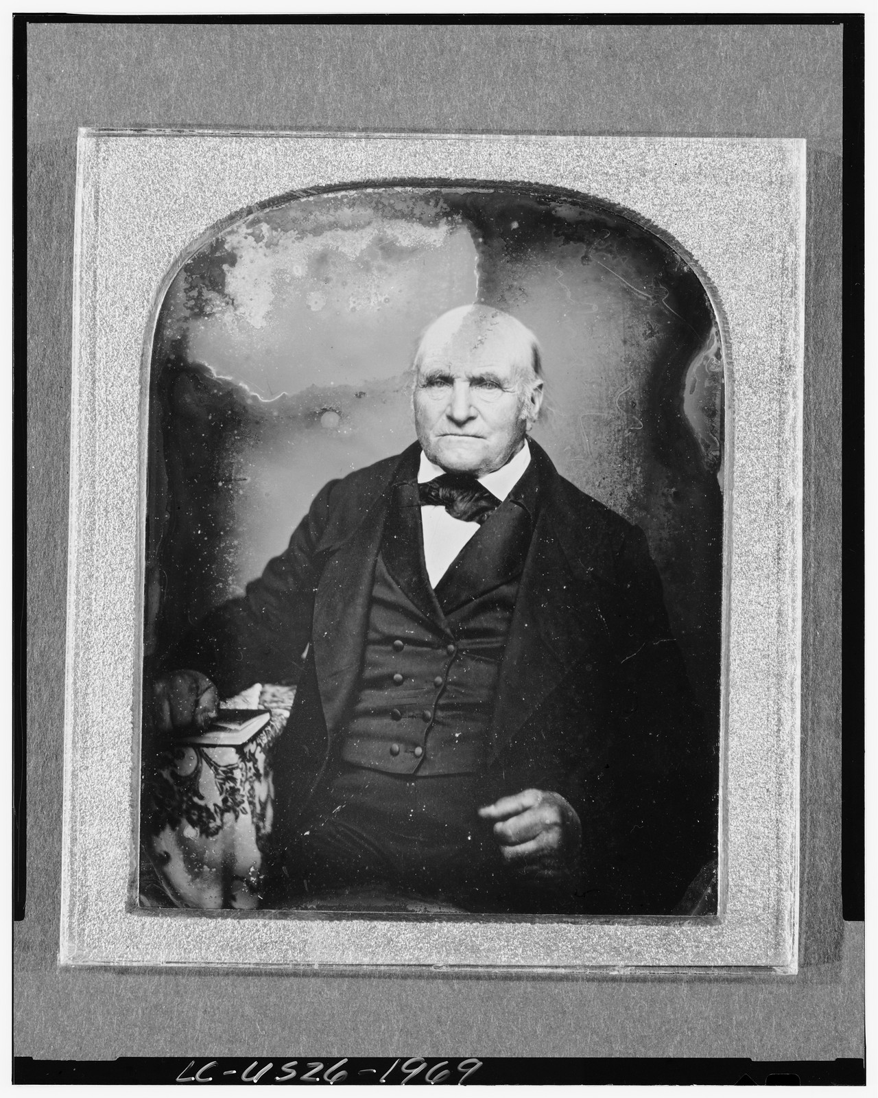 [Unidentified man, three-quarter length portrait, facing front, seated beside table with tablecloth, holding book], [between 1842 and 1860] — historic photograph
