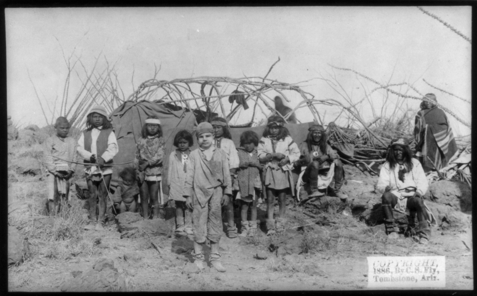 [The captive white boy, Santiago McKinn in Geronimo's Camp, with group of Indians, mostly children, in front of partially constructed tent, before Geronimo's surrender to Gen. Crook, March 27, 1886], c1886. — historic photograph