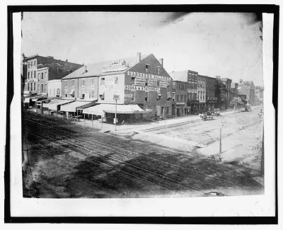 Photograph of city street with railroad tracks and shops