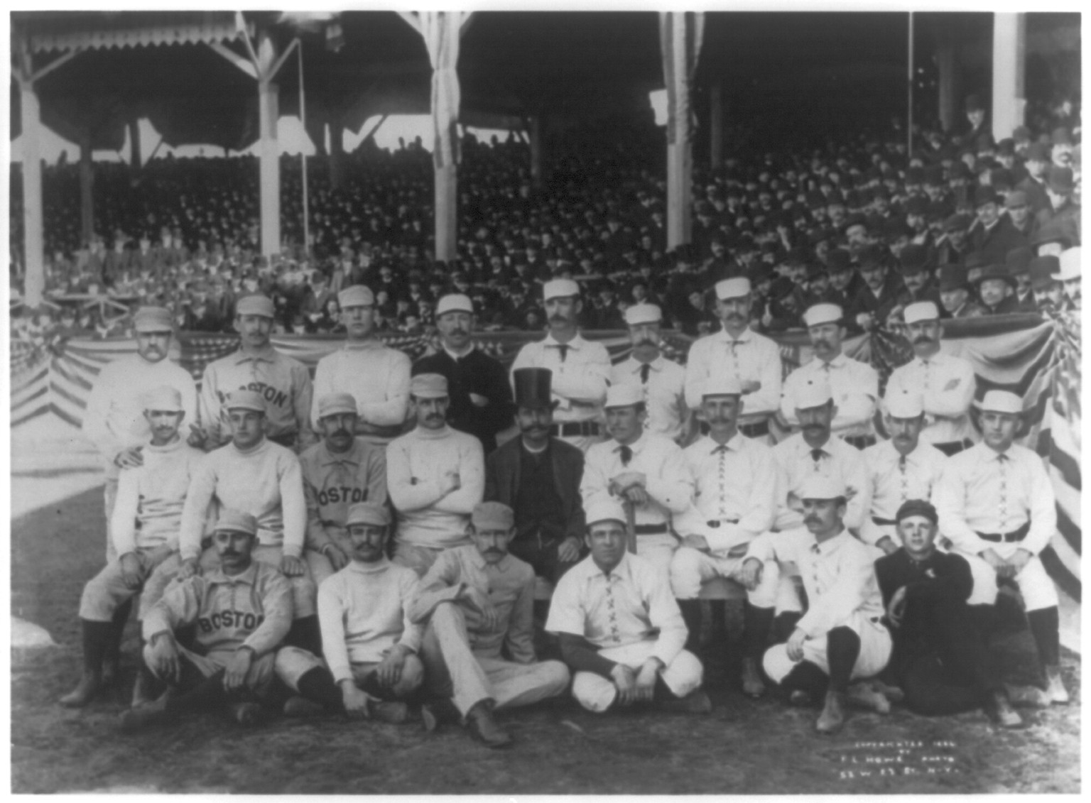 [Boston and New York players on opening day, 1886, at the Polo Grounds, 5th Ave. & 110th St., N.Y.C. posed in front of stands; Boston player in back rowon left has his middle finger raised in obscene gesture], c1886. — historic photograph