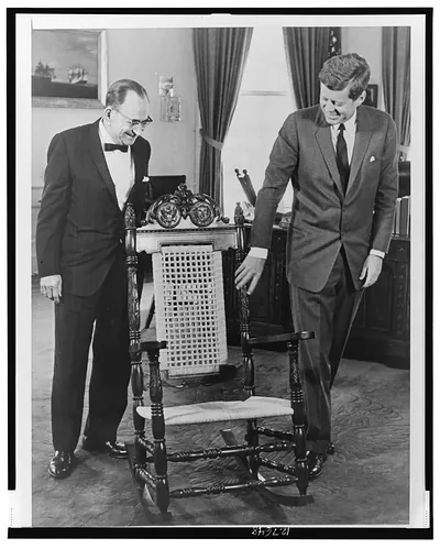 [President John F. Kennedy examines mahogany rocking chair given by Dominican Republic, as Foreign Minister of the Dominican Republic Dr. José A. Bonilla Atiles (l) looks on]