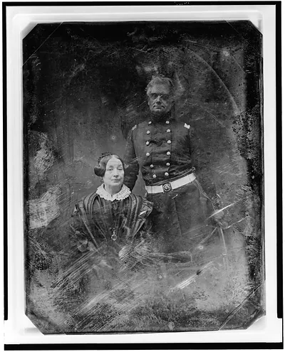 [Military officer and a woman, the officer in uniform, standing, facing front, the woman seated, on the left, nearly full face]