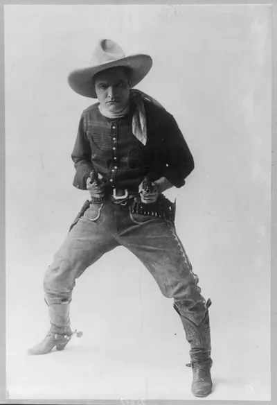 [Tom Mix, 1880-1940, full-length portrait, standing, facing left, holding 2 revolvers]