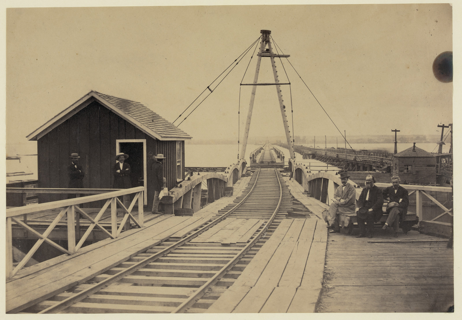 Railroad bridge trestle with derrick and seated men — historic image