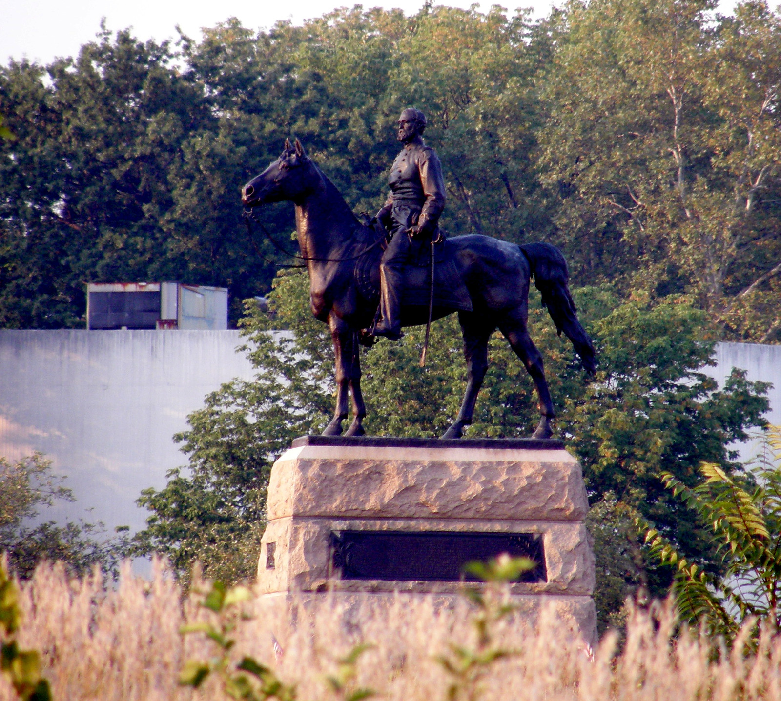 Bronze equestrian statue on granite pedestal among trees — historic image