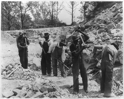 [Prisoners breaking up rocks at a prison camp or road construction site]