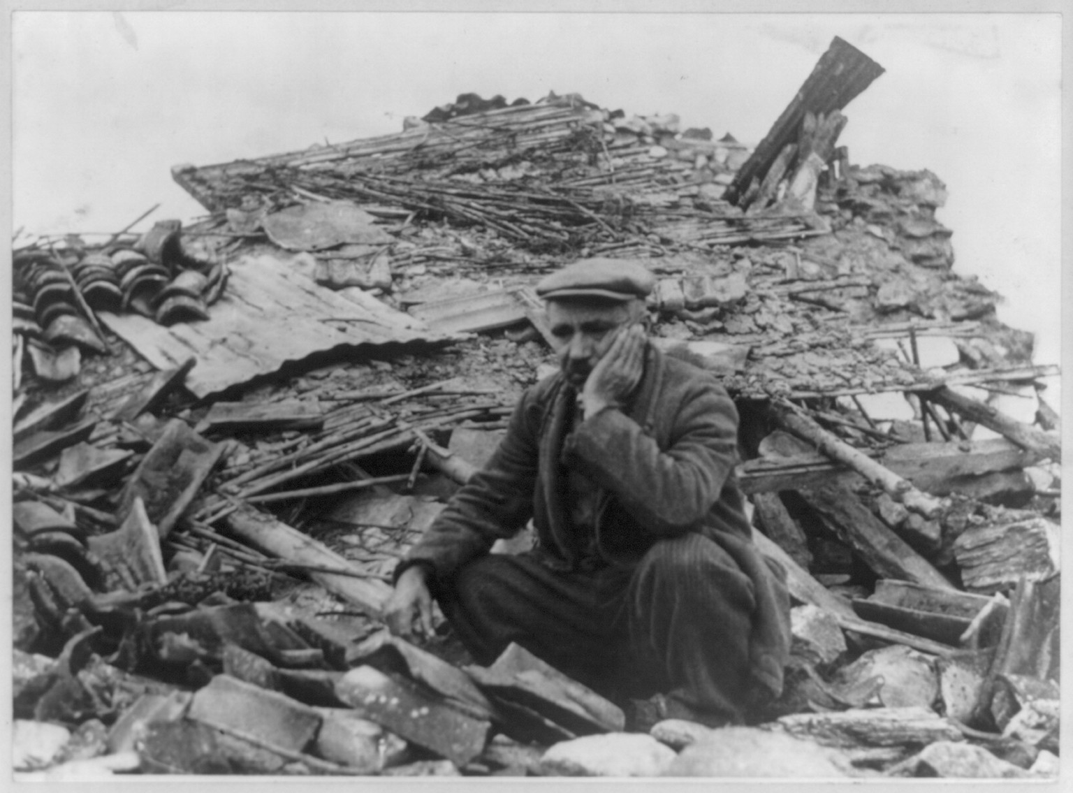 Man seated on pile of debris, after an earthquake — historic photograph
