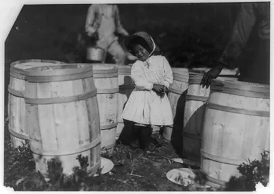 Young girl in white dress standing among wooden barrels