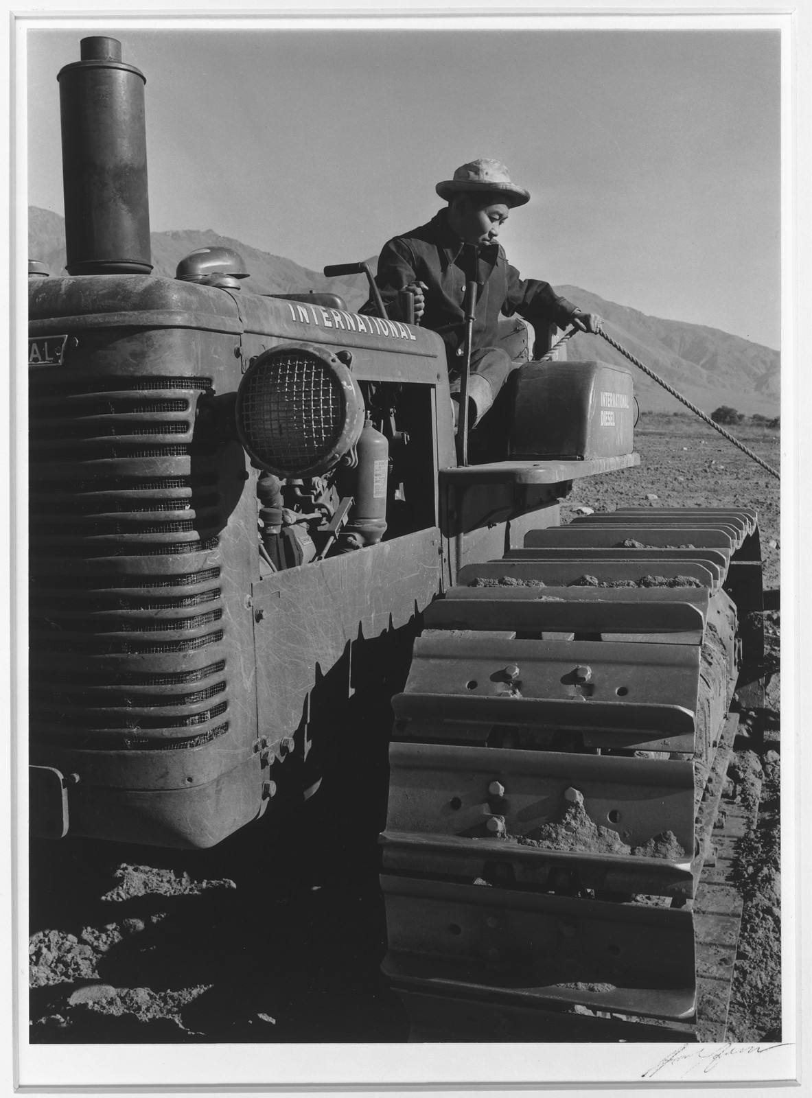 Man operating an International diesel crawler tractor on desert ground — historic image