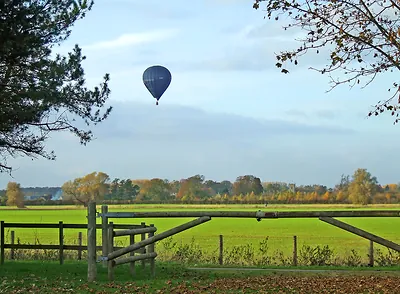 Hot air balloon over green pasture behind wooden gate