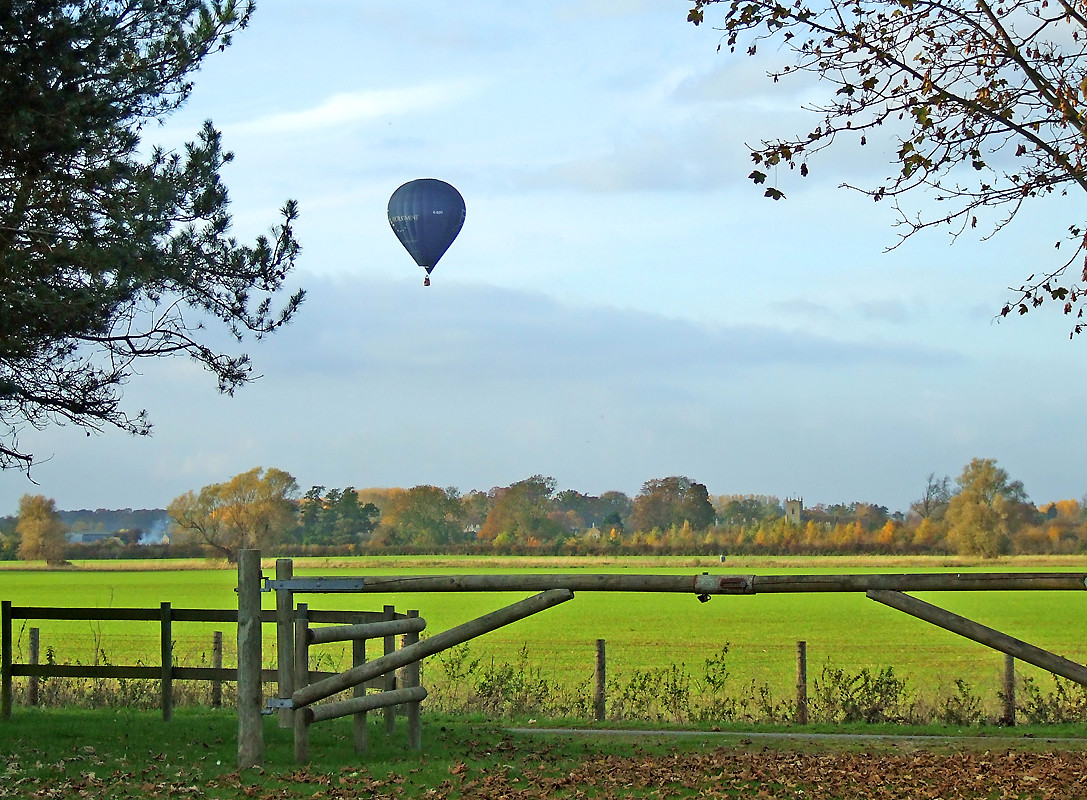 Hot air balloon over green pasture behind wooden gate — historic image