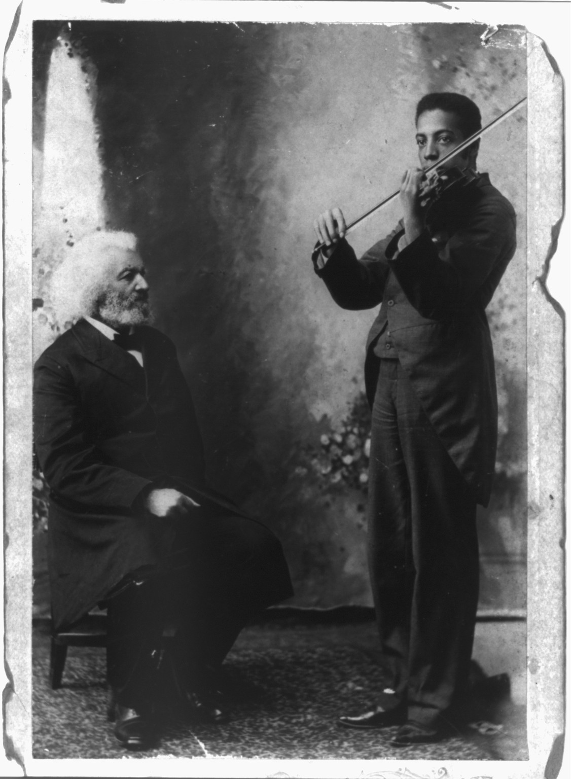 [Frederick Douglass, full length, seated beside grandson who is playing violin; facing right] — historic photograph
