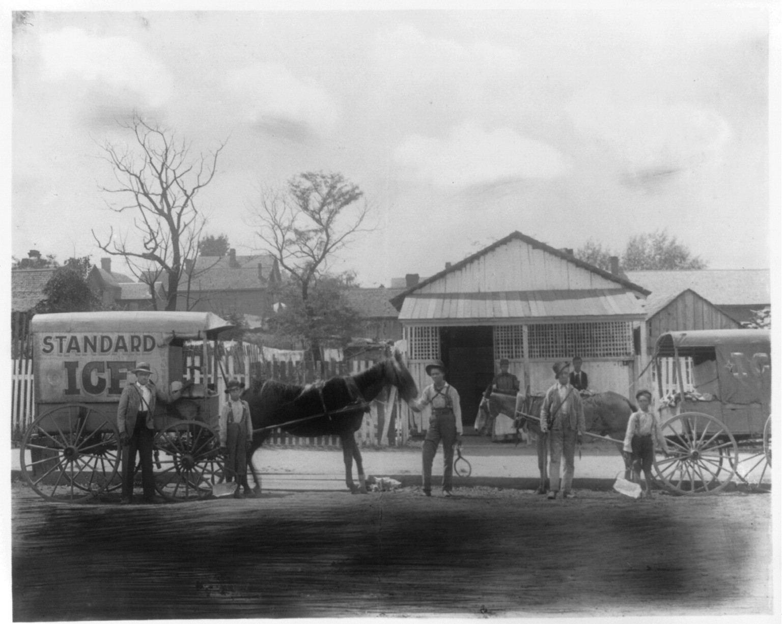 [Horse-drawn ice wagon and several persons, two with blocks of ice, standing in street in front of residence], [1899 or 1900] — historic photograph