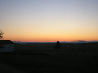 Sunset over rural fields with barn and distant hills