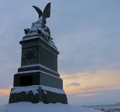 Snow-covered granite monument topped with an eagle at dusk