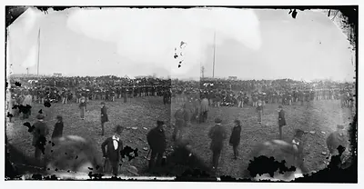 Large crowd of men on open field, Gettysburg, with flagpoles