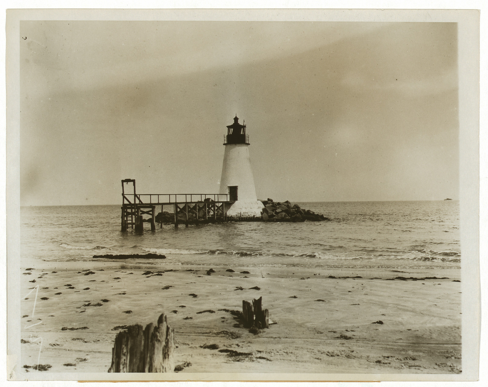 Lighthouse on a wooden pier with sandy beach — historic image