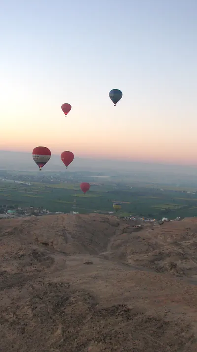 Hot air balloons over farmland and desert hills at dawn