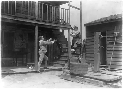 [Man in knickers with open arms to Irish Rosie" descending wooden staircase]"