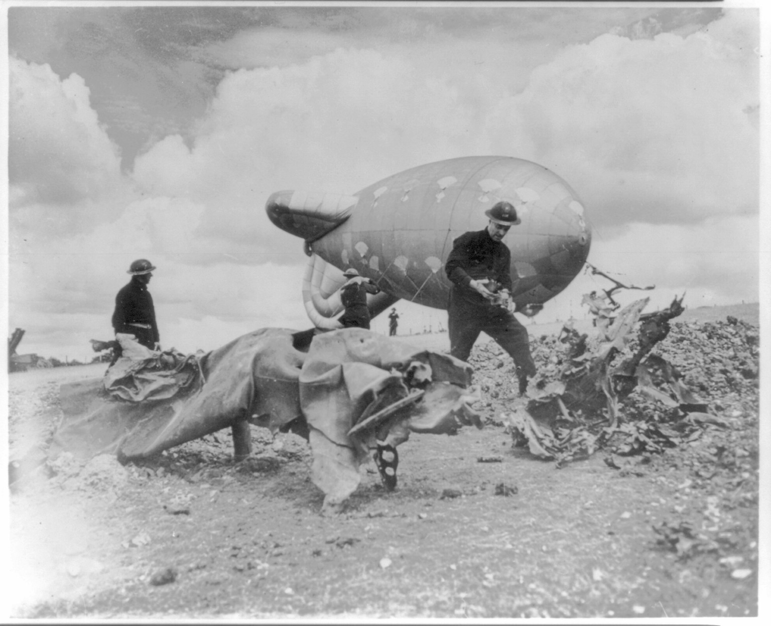 Crewmen of one of RAF's balloons in Southern England inspect wreckage of a flying bomb stopped by the cable of their barrage balloon — historic photograph