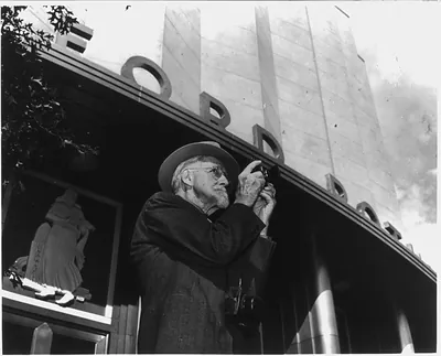 [William Henry Jackson, 1843-1942, half-length portrait, standing in front of building, facing right, holding camera]
