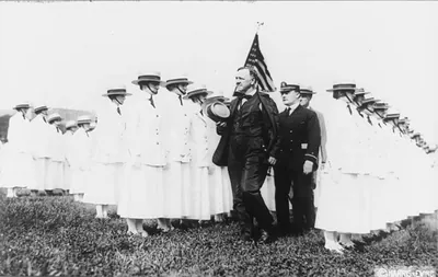 [Josephus Daniels, full-length, facing left, walking between rows of yeomanettes as they are being dismissed; an officer and Franklin D. Roosevelt are walking behind him]