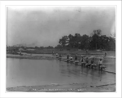 [World's Columbian Exposition, Chicago, under construction: Landscape employees pushing wheelbarrows across body of water]