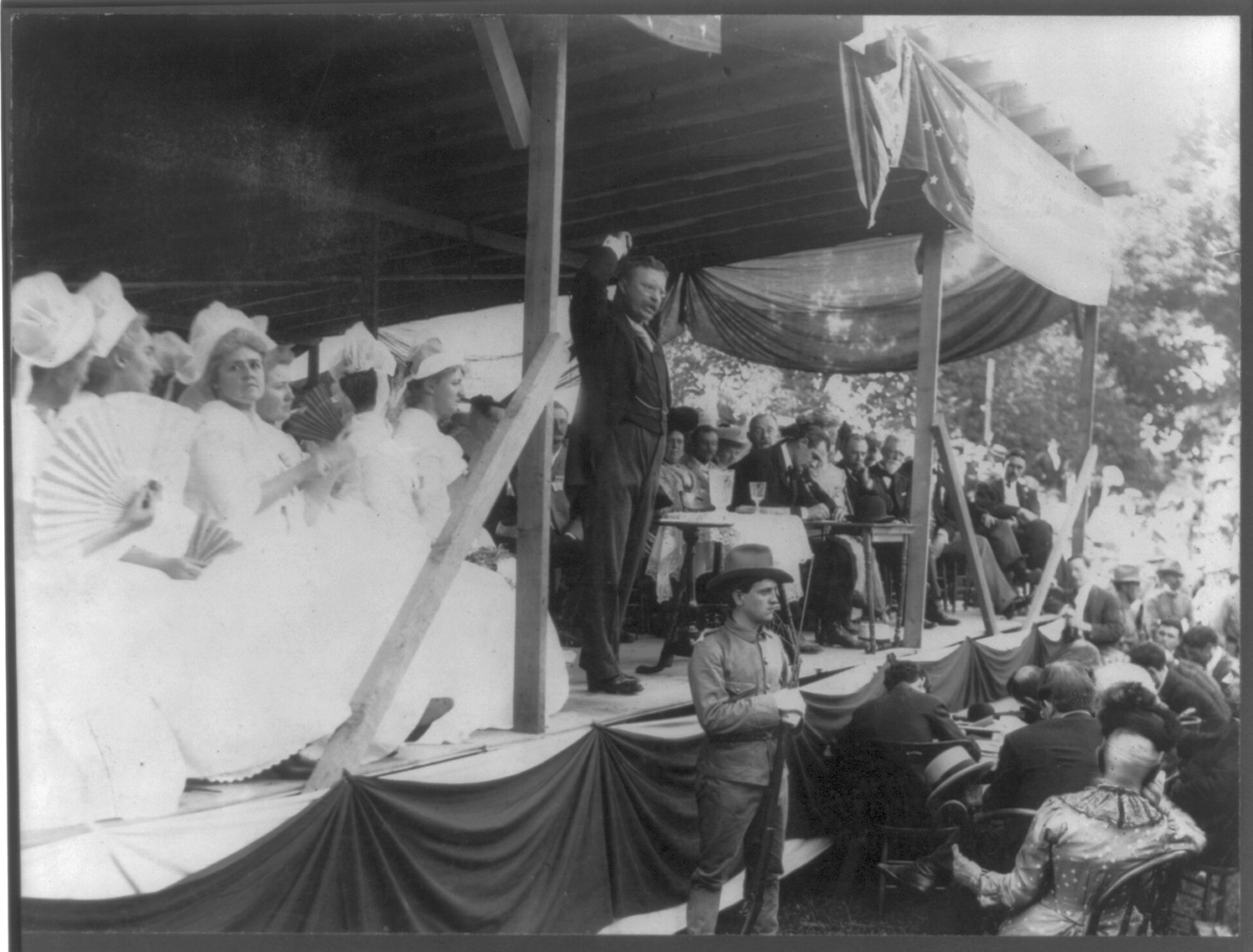 [Theodore Roosevelt, 1858-1919, full, standing, speaking from platform with upraised right arm; soldier with fixed bayonet below] — historic photograph
