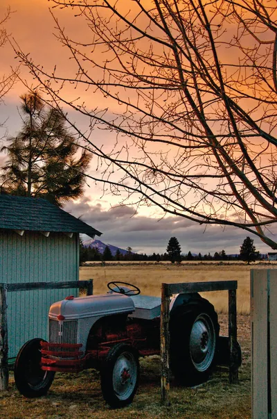 Vintage red and gray tractor beside a barn at sunset