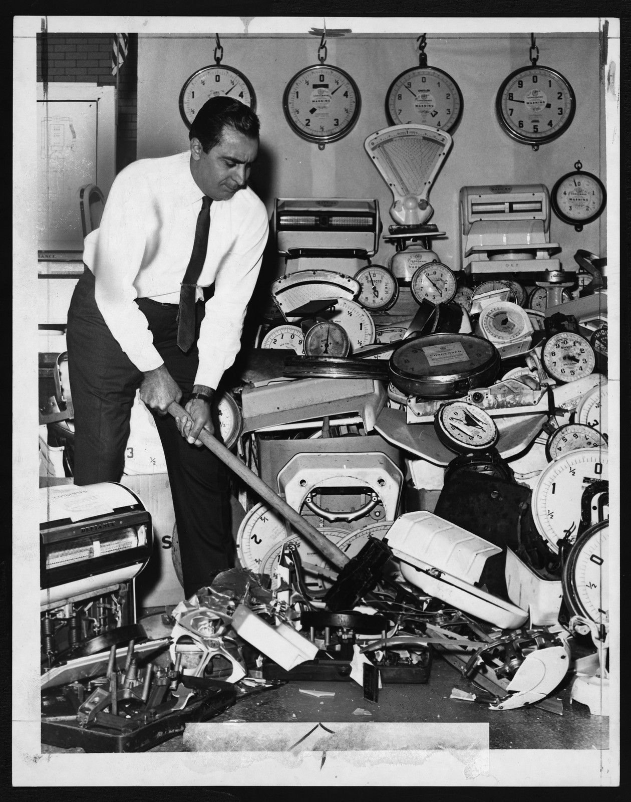 Man with sledgehammer smashing a pile of old scales — historic image