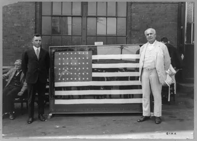 [Mr. Thomas A. Edison standing next to flag presented to him for the forty-third anniversary of the Ediphone invention by Ediphone Distributors]