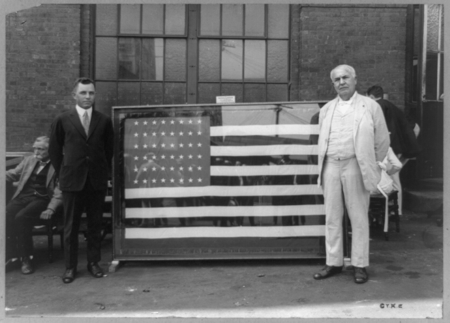 [Mr. Thomas A. Edison standing next to flag presented to him for the forty-third anniversary of the Ediphone invention by Ediphone Distributors], c1920. — historic photograph