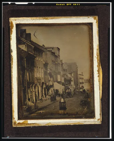 Daguerreotype of a city street with shops and carriages
