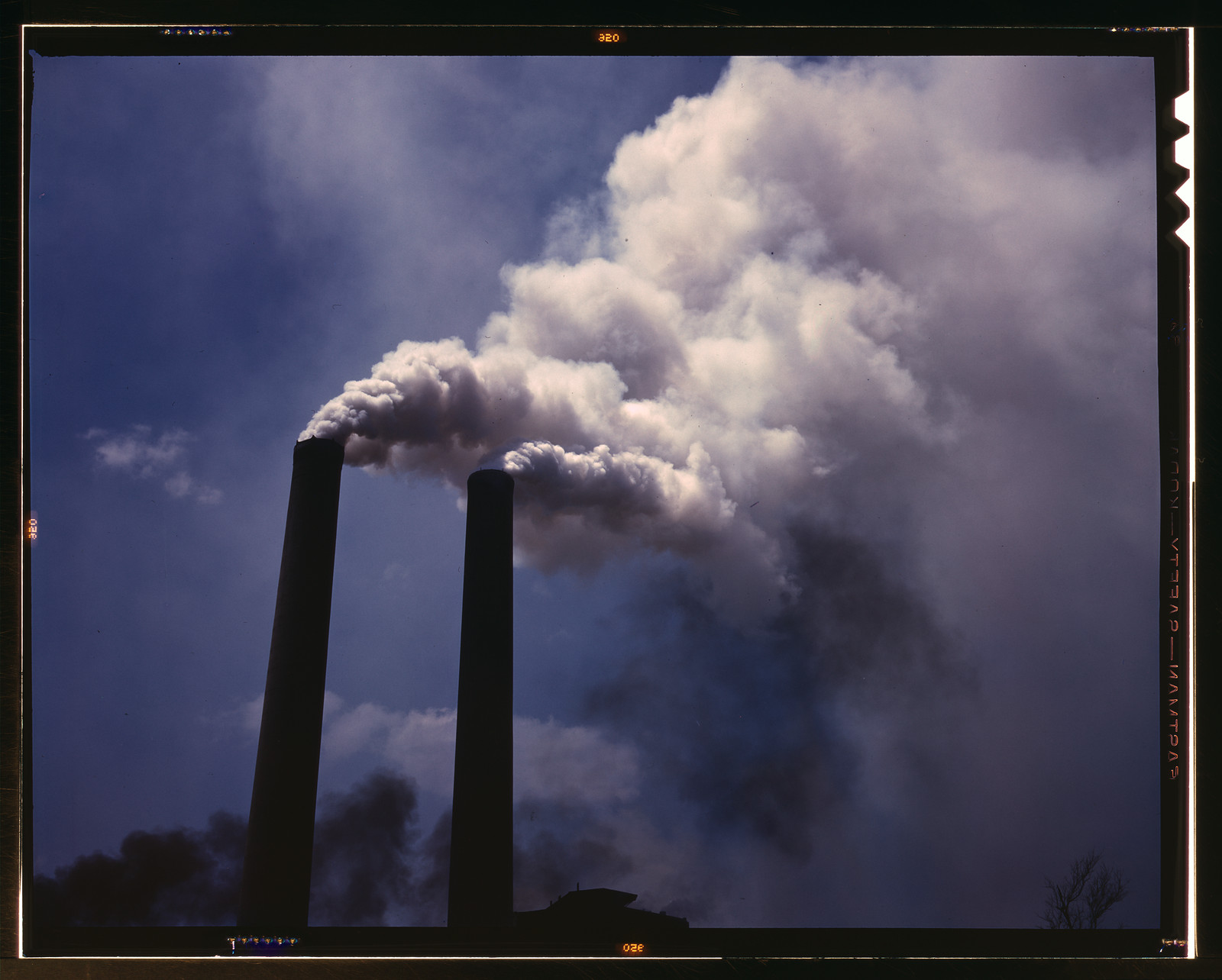 Two smokestacks emitting white smoke against a blue sky — historic image
