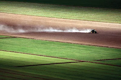 Tractor raising dust across a plowed farm field