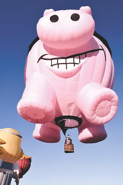 Pink pig-shaped hot air balloon against a blue sky