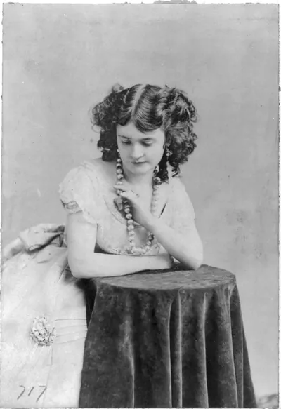 [Lotta Crabtree, half-length portrait, facing left, leaning on table, looking down]