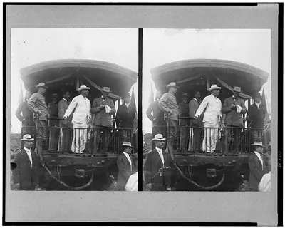 [Theodore Roosevelt, standing on back of railroad car, speaking toward crowd]