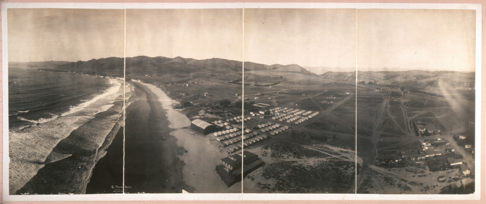Panoramic aerial view of coastal beach and tent camp — historic image