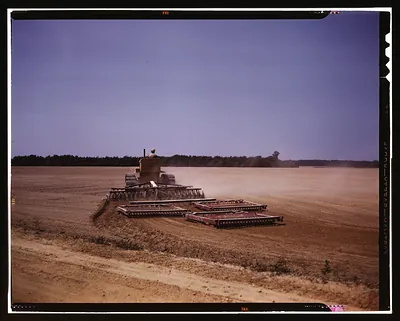 Tractor pulling disc harrows across a dusty field