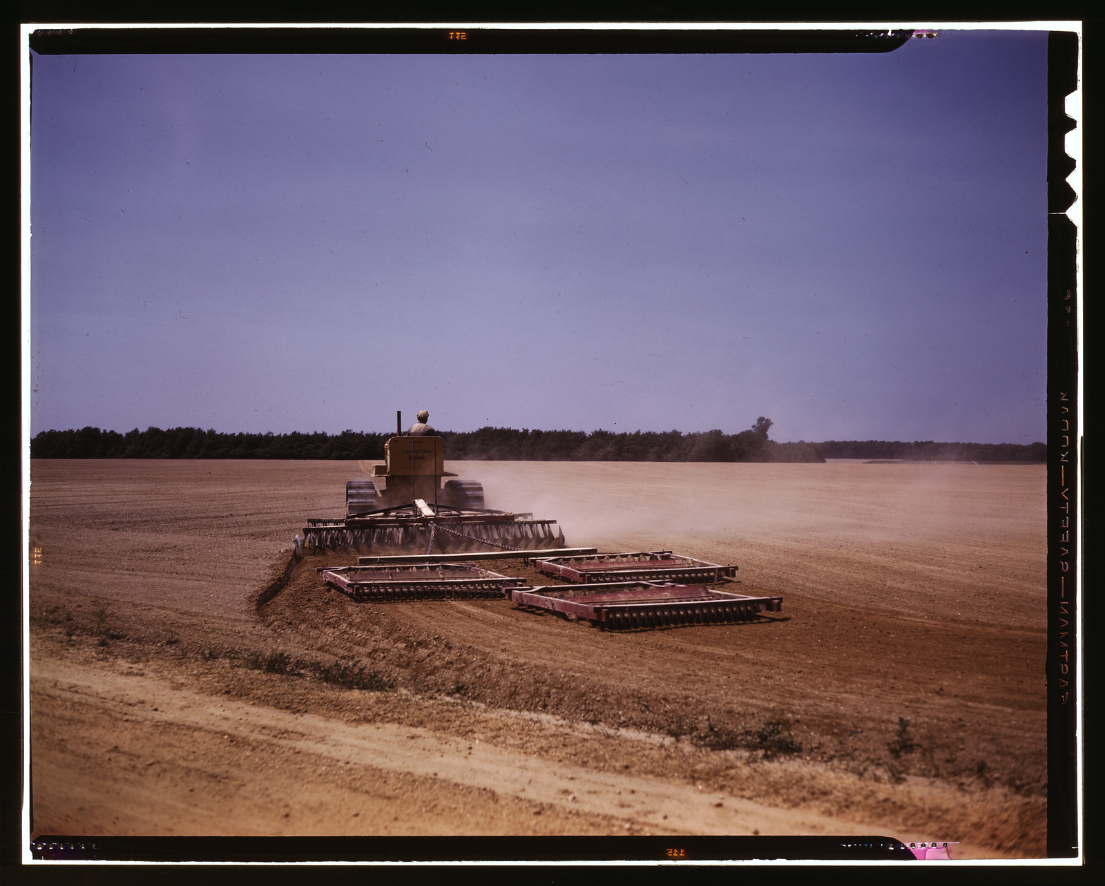 Tractor pulling disc harrows across a dusty field — historic image