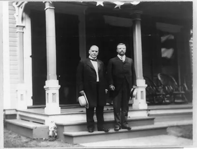 [William McKinley and Theodore Roosevelt standing on step of porch]