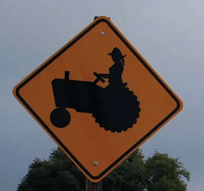 Yellow diamond warning sign with tractor and woman driver silhouette