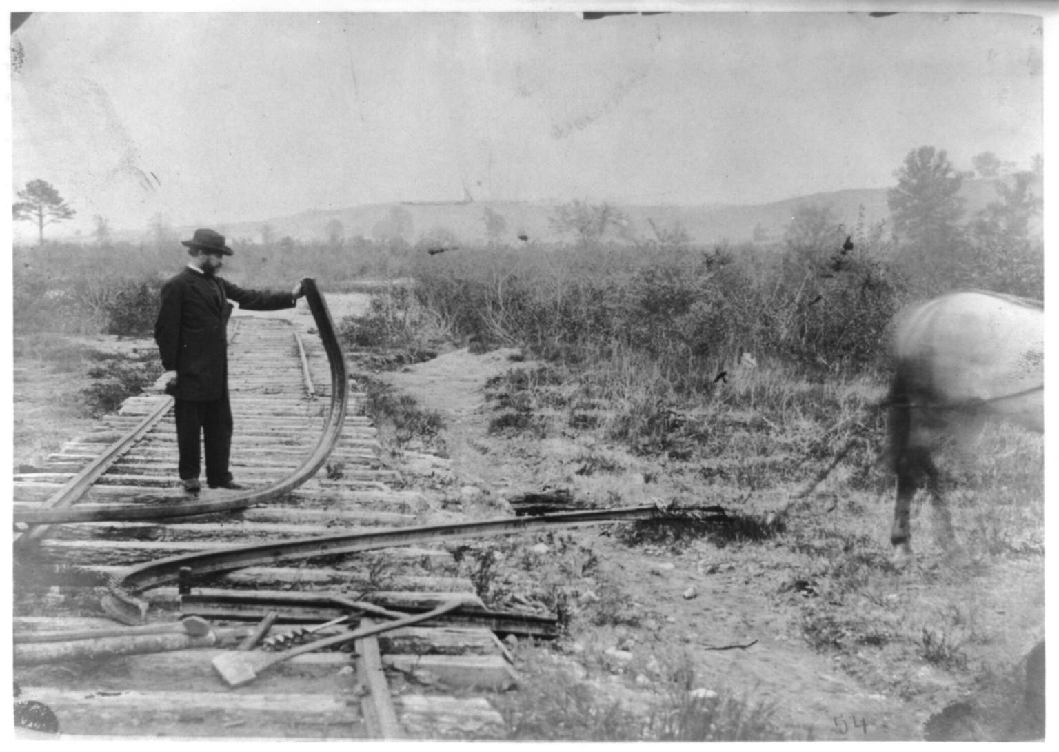 [Military railroad operations in northern Virginia: man standing on railroad tracks holding twisted rail], [1862 or 1863] — historic photograph