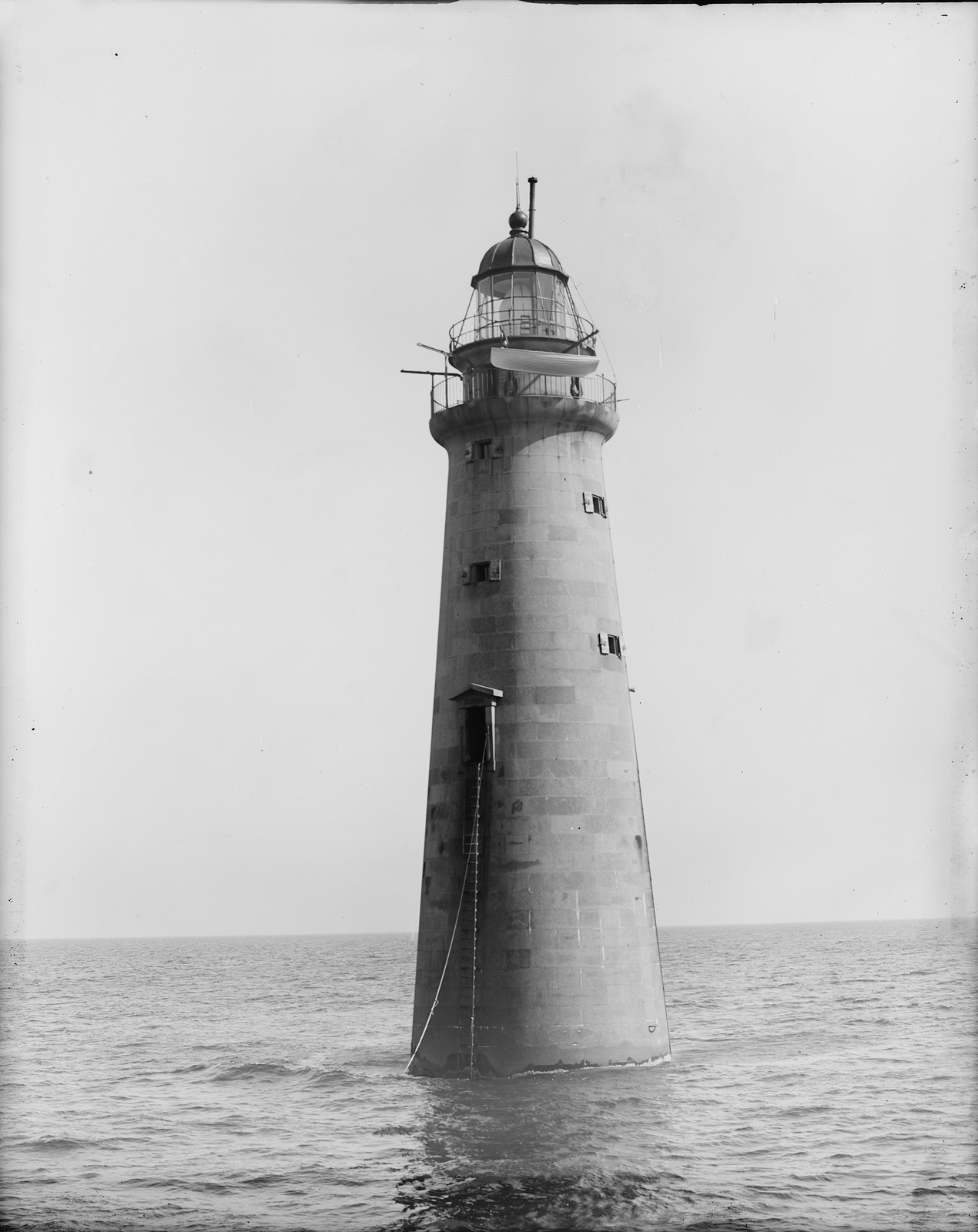 Tapered stone lighthouse rising from calm open sea — historic image